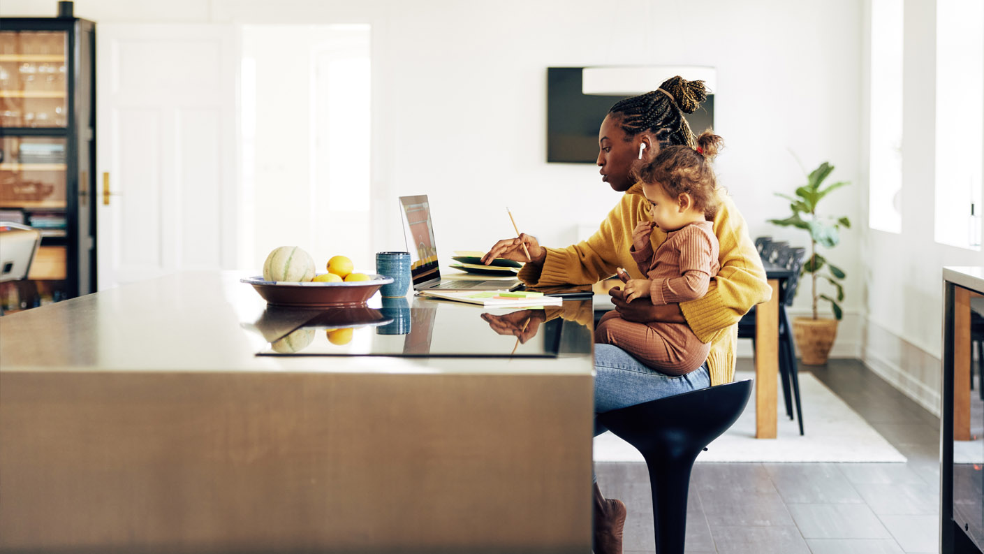 Remote working. Woman working at a kitchen table with a child sitting on her knee